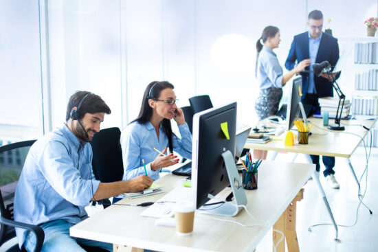 Attractive business people in headsets are smiling while working with computer in modern office