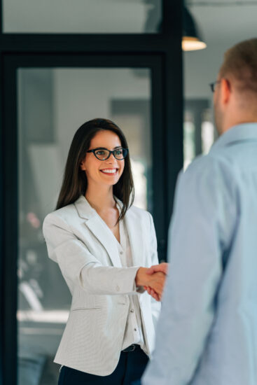 Smiling businesswoman handshake with businessman while standing in the office.