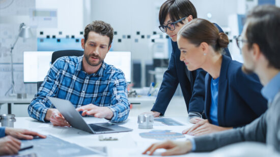 Factory Meeting Room: Multi-Ethnic and Diverse Team of Engineers, Managers, Investors Talking Sitting at Conference Table, Analyzing Blueprints, Mechanism Component. High-Tech Manufactory Optimization